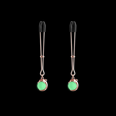 Rose gold adjustable nipple clamps with soft black silicone tips and green decorative accents on a black background.