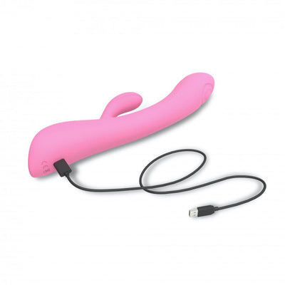 Pink dual stimulator with curved design and clitoral arm, shown with USB charging cable on white background.