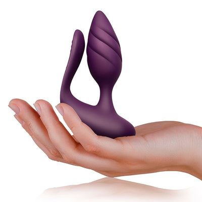 Hand holding a purple dual-motor couples vibrator with textured and flexible silicone design.