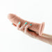 Hand holding a beige dual density dildo with a suction cup base against a white background.