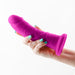 Hand holding a purple dual density dildo with a suction cup base against a white background.