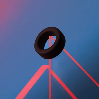 Black liquid silicone cockring displayed on a geometric blue and pink background.
