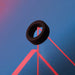 Black liquid silicone cockring displayed on a geometric blue and pink background.