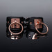 Pair of black vegan leather cuffs with rose gold metal rings and engraved Coquette plates on reflective black surface.