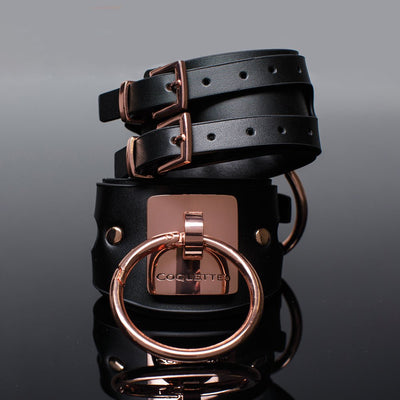 Black vegan leather cuffs with rose gold metal buckles and large O-ring, featuring Coquette engraving and adjustable straps.
