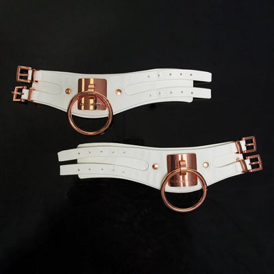 White vegan leather adjustable cuffs with rose gold metal O-rings and buckles, featuring Coquette engraved plates.