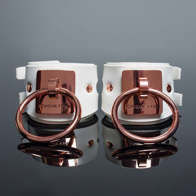 White vegan leather cuffs with rose gold metal rings and engraved Coquette plates, adjustable buckle closures.