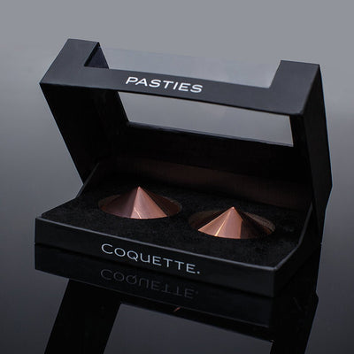 Coquette Pleasure Collection rose gold metal pasties in black velvet-lined display box with clear lid and ribbon loop.