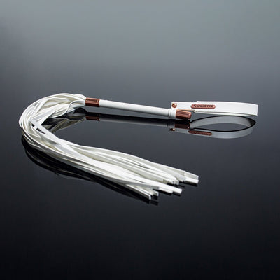 White vegan leather whip with multiple tails, rose gold accents, and adjustable wrist strap on reflective black surface.