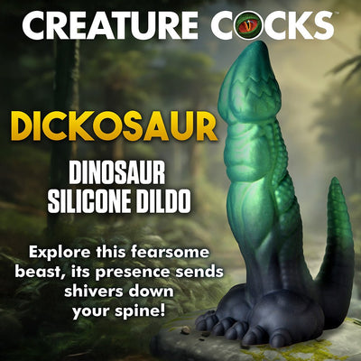 Green and black textured dinosaur-themed silicone dildo with clawed feet and a curved tail on a forest floor background.