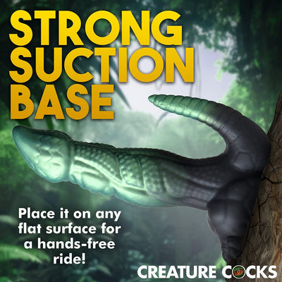 Green and black textured dinosaur-themed adult toy with suction cup base mounted on a tree trunk for hands-free use.