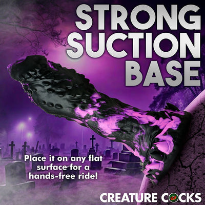 Black and purple textured dildo with strong suction base shown against a misty graveyard background.