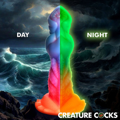 Colorful Creature Cocks Aqua dildo shown glowing green in the dark and vibrant in daylight against an ocean background.
