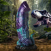Blue and purple glittery dinosaur-themed silicone dildo with textured base and tail in a jungle setting.