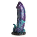 Large fantasy dildo in shimmering blue, purple, teal, and black with dinosaur-inspired textured base and suction cup.