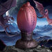 Dragon egg-shaped silicone plug in red and purple hues with textured ridges, set against a fantasy mountain and dragon background.