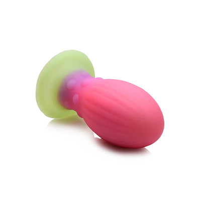 Large silicone glow-in-the-dark egg-shaped plug in pink, purple, and green with ribbed texture and bumpy neck.