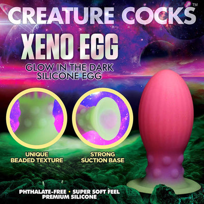 Glow-in-the-dark pink and green silicone egg with textured beaded sides and suction base on a cosmic background.