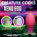 Glow-in-the-dark pink and green silicone egg with textured beaded sides and suction base on a cosmic background.
