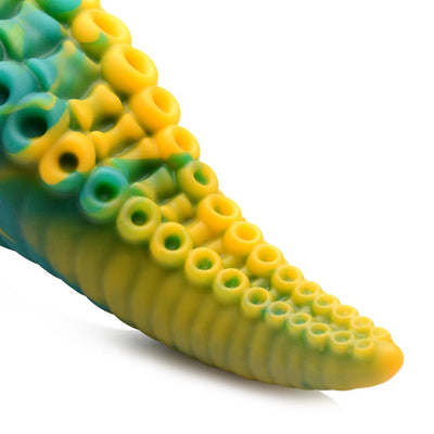 Close-up of green and yellow silicone tentacle dildo with detailed suction cups on textured surface.