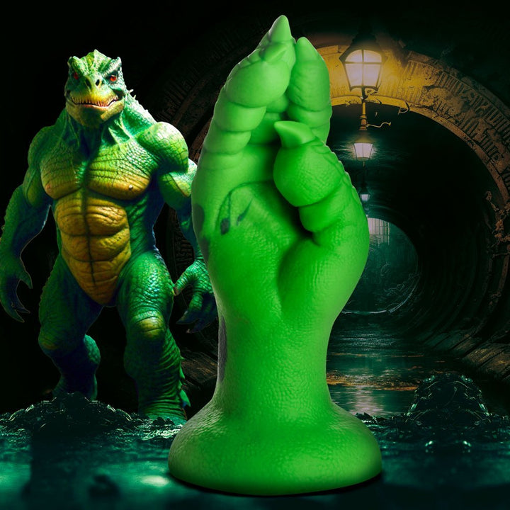 Green silicone dildo shaped like a raptor claw with textured scales and a wide suction cup base against a dark tunnel background.