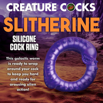 Purple silicone cock ring shaped like a spiked, toothy alien worm against a desert sci-fi background.