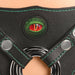 Close-up of black vegan leather strap-on harness with green stitching, creature eye detail, and metal O-ring.