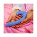 Hands holding a curved blue silicone dual-ended intimate toy on a soft pink blanket background.