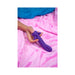 Hand holding a purple ergonomic vibrator with fins on a soft pink blanket background.