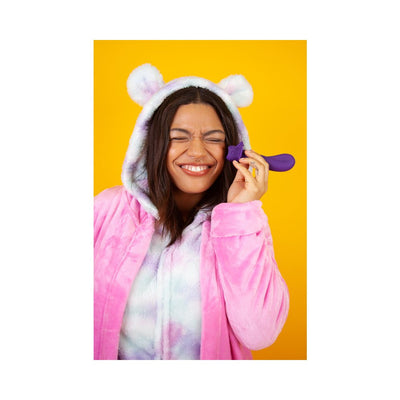 Smiling woman in a pastel pink and purple hooded robe holding a purple ergonomic vibrator against a bright yellow background.