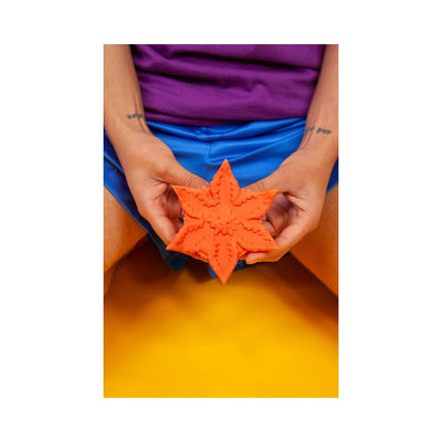 Hands holding a textured, star-shaped rose-colored silicone companion against a vibrant yellow background.