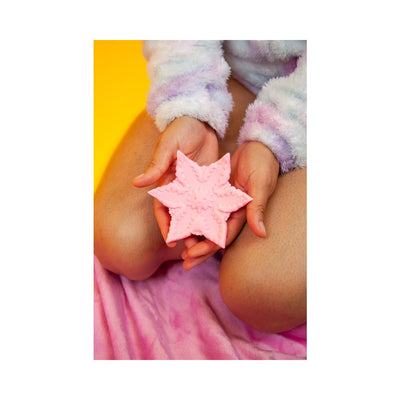 Hands holding a pink star-shaped textured silicone companion on a pink blanket with a yellow background.
