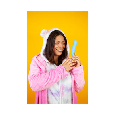 Smiling woman in a pink and white fuzzy hoodie holding a teal curved personal massager against a yellow background.