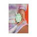 Hand holding a mint green insect-shaped silicone vibrator against a soft pastel purple and white fuzzy outfit.