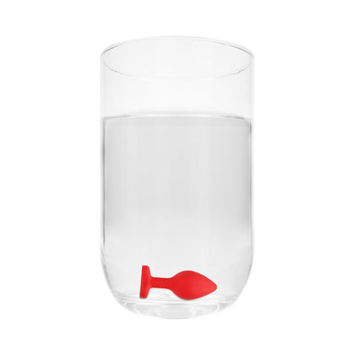 Large red silicone butt plug with diamond-shaped base submerged in clear water in a glass.