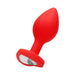 Large red silicone butt plug with tapered shape and clear diamond-shaped gem at the flared base.