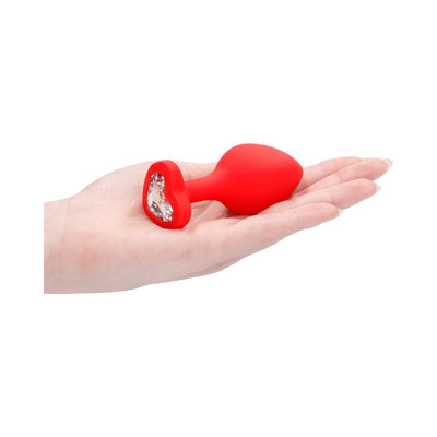 Hand holding a large red silicone butt plug with a heart-shaped base adorned with a clear diamond-like gem.