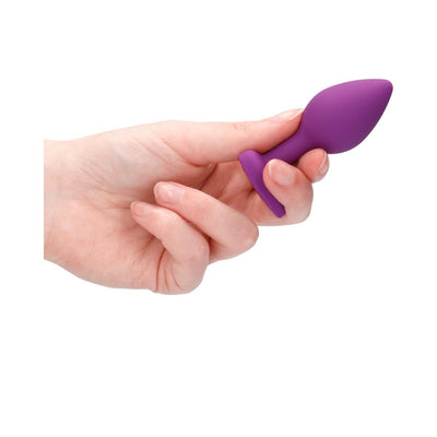Hand holding a small purple silicone butt plug with a flared base and diamond detail.