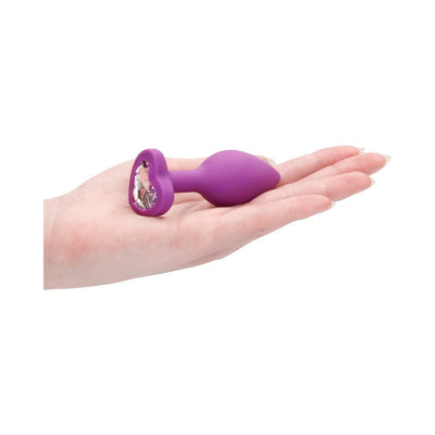 Hand holding a purple silicone butt plug with a heart-shaped base featuring a clear diamond detail.