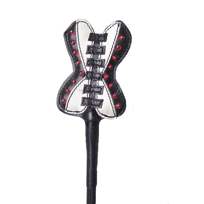 Close-up of a leather crop tip shaped like a black and white corset with red studs and black lacing details.