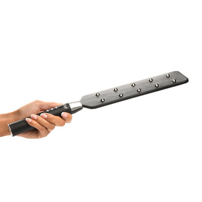 Hand holding a black vegan leather paddle with metal spikes and a control handle for adjustable e-stimulation intensity.