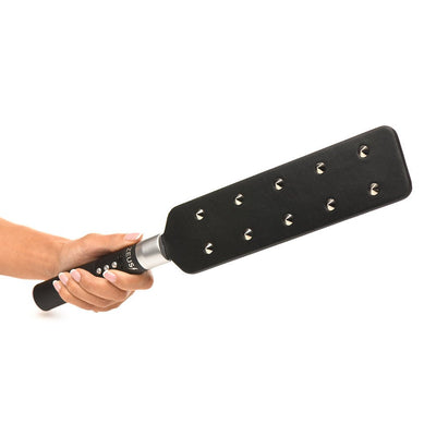 Hand holding a black e-stim paddle with ten metal spikes on one side and control buttons on the handle.