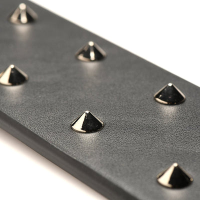 Close-up of black vegan leather paddle with shiny metal spikes for e-stim sensation play.