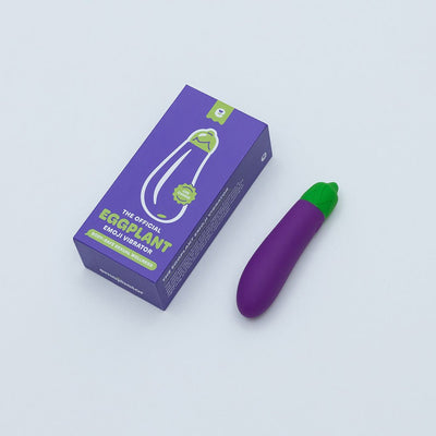 Purple eggplant-shaped vibrator with green top next to its purple and green packaging box on a white background.