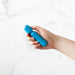 Hand holding a compact blue Emojibator Tiny Wand vibrator with textured grip against a white background.