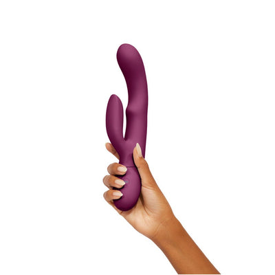 Hand holding a deep purple silicone dual-stimulation rabbit vibrator with curved design and control button.