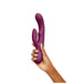 Hand holding a deep purple silicone dual-stimulation rabbit vibrator with curved design and control button.