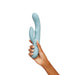 Hand holding a light blue silicone dual-stimulation rabbit vibrator with curved shaft and smaller clitoral arm.