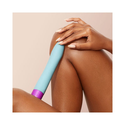Close-up of a hand holding a blue and purple flexible bullet vibrator resting on a bent knee against a neutral background.