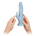 Hands holding a light blue silicone dual-stimulation Turbo Rabbit vibrator with flexible clitoral arm and suction base.